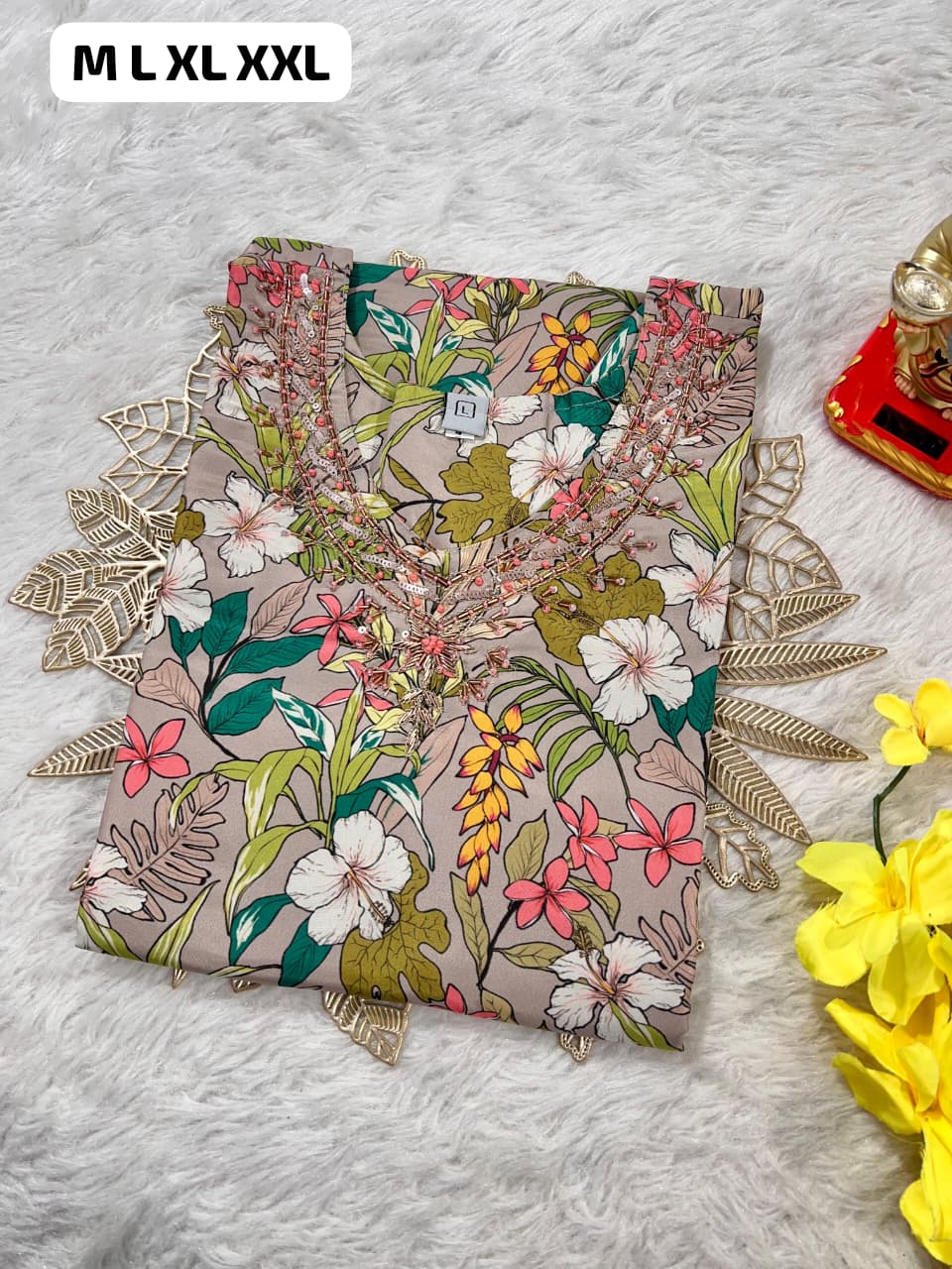 folded floral print kurti with bead embroidery on beige fabric beside yellow flowers on soft white surface