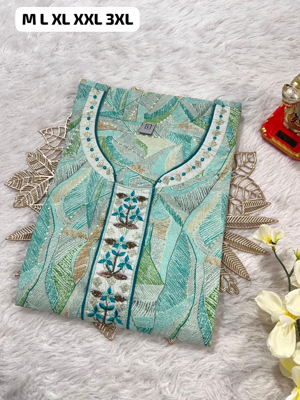 Folded blue and green embroidered kurta with floral and leaf patterns on white fabric background