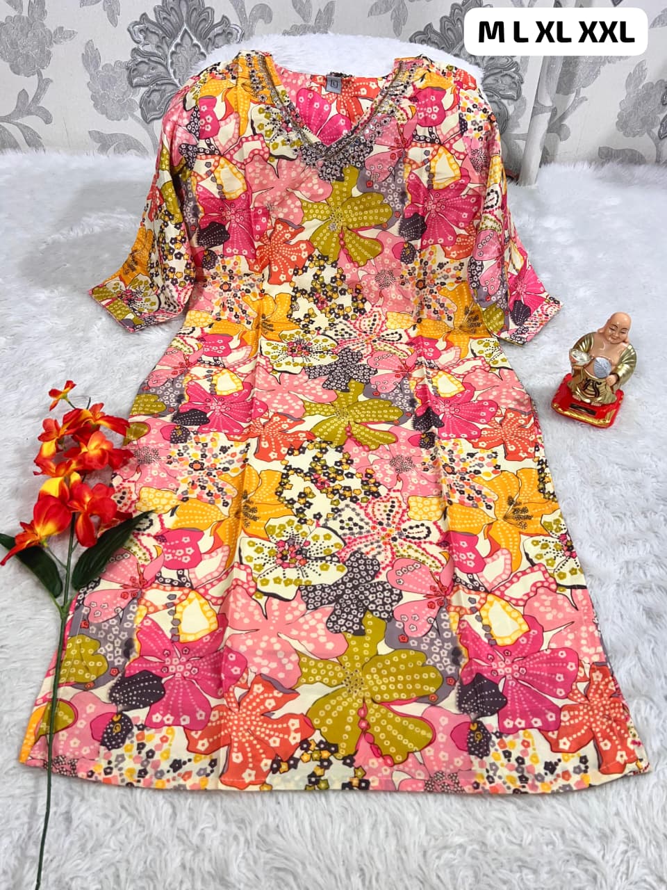 colorful floral print dress with V-neck and 3/4 sleeves displayed on white fur with red flowers and small Buddha statue